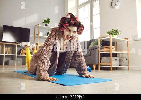 Bonne jeune femme qui fait des push-up de genou sur le tapis d'exercice pendant entraînement physique à la maison Banque D'Images