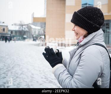 Jeune femme souriante tenant une tasse sur une promenade l'hiver jour Banque D'Images