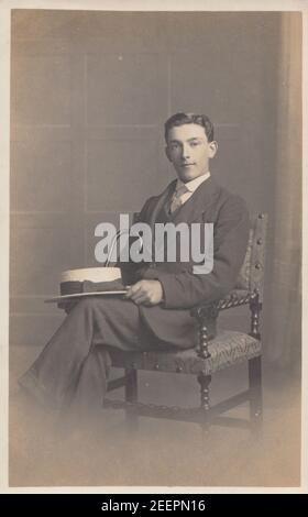 Carte postale photographique vintage du début du XXe siècle montrant un portrait de studio d'un Smart Young Man Sat dans une chaise tenant une canne et un chapeau de bateau. Banque D'Images