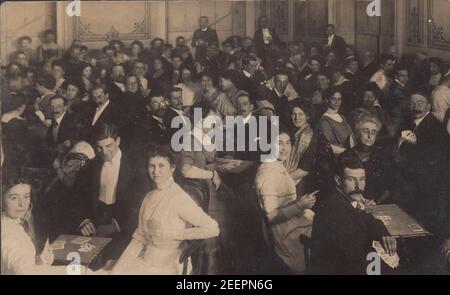 Carte postale photographique édouardienne vintage montrant un grand groupe de personnes bien habillées jouant aux cartes. On croyait être une soirée de whist Drive, c1910. Banque D'Images