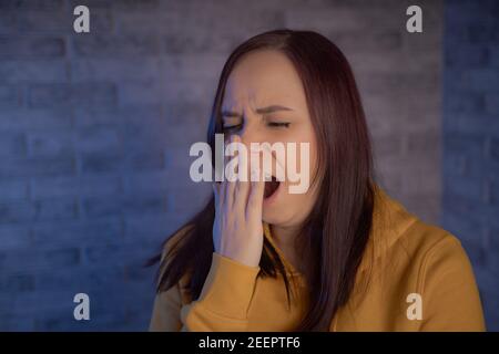 Une femme bâilleuse sur fond de mur de briques grises. La jeune brune couvre sa bouche et naine le matin Banque D'Images