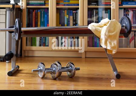 Covid fitness: fer haltères sous un banc de musculation avec une longue barbell et une serviette dans le bureau à la maison. Banque D'Images