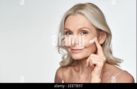 Souriante 50s moyenne d'âge mature femme appliquant de la crème sur le visage isolé sur blanc. Banque D'Images