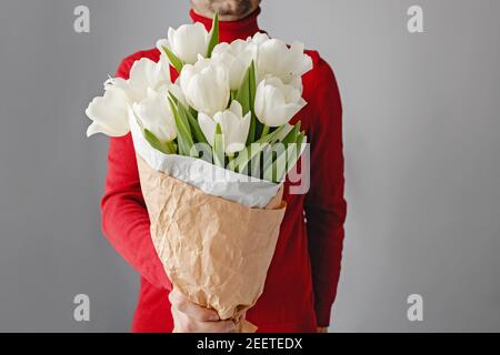 Homme en chandail rouge tenant un bouquet de tuis blanc. Banque D'Images