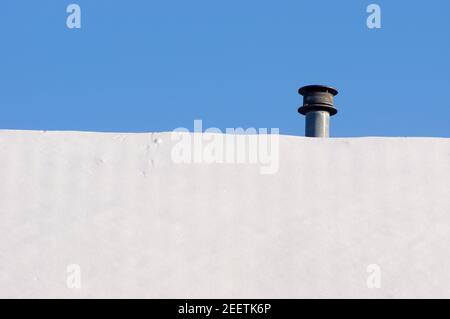 Toit avec une petite cheminée couverte de neige avec clair ciel bleu Banque D'Images