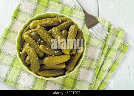 Gros plan de cornichons marinés dans un bol en céramique sur une serviette à carreaux verts sur une table. Cornichons entiers marinés avec de l'aneth et des graines de moutarde. Croquant Banque D'Images