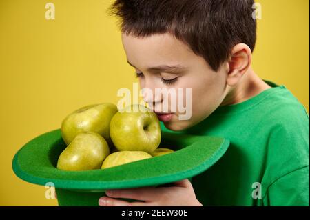 Le petit garçon mignon aime le parfum des pommes vertes dans un chapeau irlandais vert de lepretchun. Portrait du visage. Saint Patrick Banque D'Images