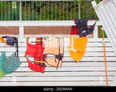 Les gilets de sauvetage rouges et orange sèchent sur une clôture en bois blanc Banque D'Images