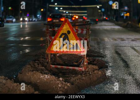 La route fonctionne devant le panneau à la nuit d'hiver rue près de la fosse - gros plan avec mise au point sélective Banque D'Images