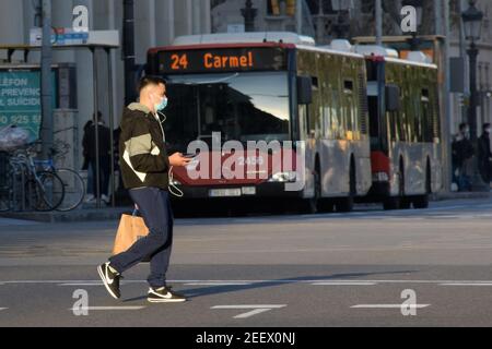 Jeune homme traversant la rue avec un masque et un téléphone portable en main pendant la pandémie de cavid.Barcelone, Catalogne, Espagne. Banque D'Images