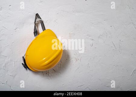 Casque de travail jaune accroché à un crochet. Accessoires de santé et de sécurité sur fond de mur blanc. Arrière-plan clair. Banque D'Images