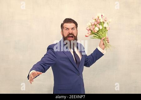 Des vacances de haine. Journée pour femme. 8 Mars. Homme barbu en colère avec des fleurs. Fêtez le printemps. Échec de la date. Irritée, l'homme barbu agacé avec bouquet de tulipes. Concept déçu. Date d'échec. Banque D'Images