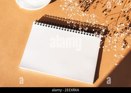 Maquette de bloc-notes vierge sur fond orange avec fleurs de gitsophila. Vue de dessus, plat, espace de copie. Banque D'Images
