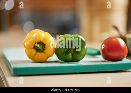 Photo en gros plan des poivrons jaunes et verts et du rouge tomate mûre sur une planche à découper Banque D'Images