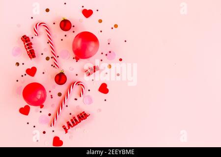 Boîte rouge avec confettis, ballons, banderoles et décoration sur fond rose. Célébration colorée, arrière-plan d'anniversaire. Flat lay, vue de dessus Banque D'Images