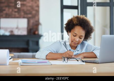 Jolie race mixte adolescence école fille regardant focalisé, en utilisant l'ordinateur portable tout en prenant des notes pendant la leçon vidéo en ligne à la maison Banque D'Images