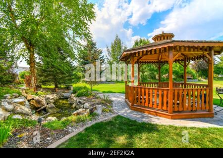 Un jardin joliment aménagé et une cour arrière avec un rond belvédère en bois de cèdre et étang avec chute d'eau Banque D'Images