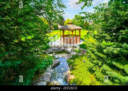 Un petit ruisseau coule vers un belvédère en bois dans un jardin paysager. Banque D'Images