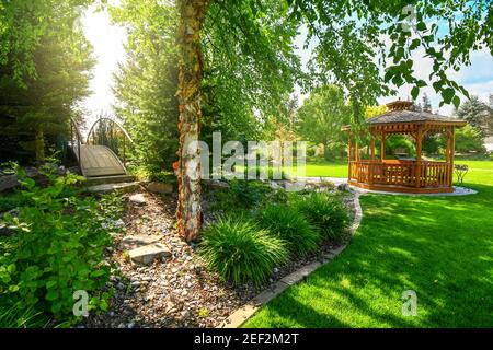 Un jardin joliment aménagé et une cour arrière avec un belvédère rond en bois de cèdre et un pont sur d'autres espaces paysagers. Banque D'Images