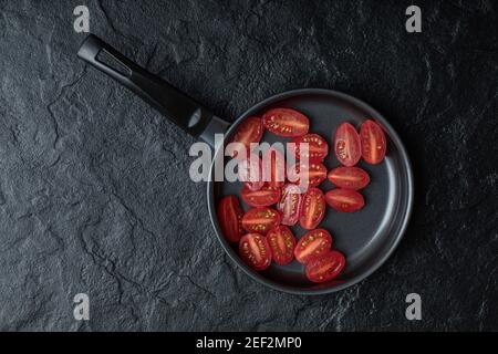 Couper à moitié les tomates cerises fraîches sur la poêle noire arrière-plan noir Banque D'Images