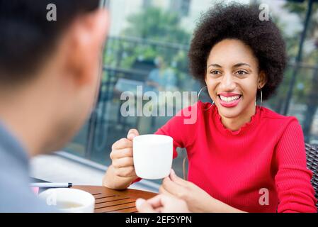 Souriante décontractée Afro-Caribbean femme buvant un café avec un ami à l'intérieur café-restaurant Banque D'Images