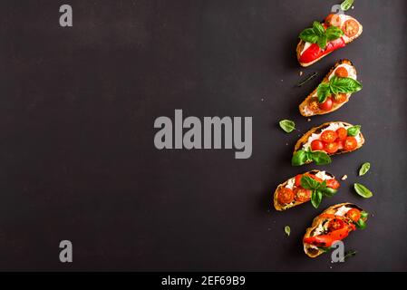 Sandwichs à la bruschetta avec tomates, fromage à la crème, paprika grillé et basilic sur fond sombre, vue du dessus, espace de copie. En-cas italien traditionnel pour W Banque D'Images