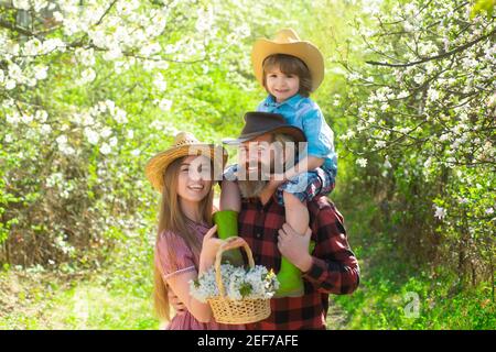 Une famille joyeuse pique-nique dans un parc. Agriculteurs familiaux travaillant dans le jardin des arbres au printemps. Père mère et enfant travaillent dans la cour avec des outils de jardinier. Banque D'Images