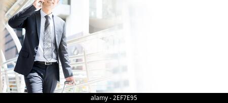 Businessman calling on cell phone tout en tirant des bagages et marche dans une allée couverte, vue panoramique sur copy space Banque D'Images