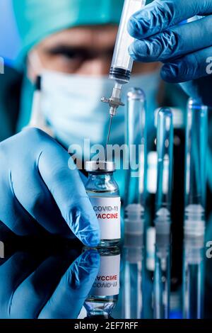 Médecin avec des capuchons médicaux et des gants en latex prend le vaccin covid avec une seringue dans un tableau avec plusieurs flacons Banque D'Images