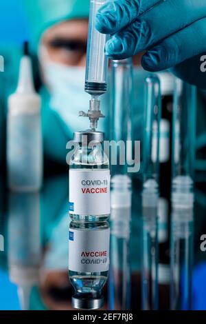 Médecin avec des capuchons médicaux et des gants en latex prend le vaccin covid avec une seringue dans un tableau avec plusieurs flacons Banque D'Images