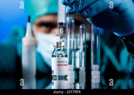 Médecin avec des capuchons médicaux et des gants en latex prend le vaccin covid avec une seringue dans un tableau avec plusieurs flacons Banque D'Images