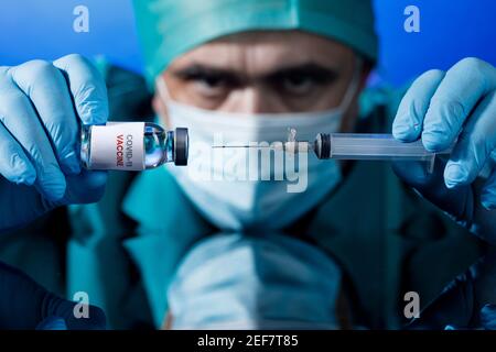 Médecin avec des capuchons médicaux et des gants en latex prend le vaccin covid avec une seringue dans un tableau avec plusieurs flacons Banque D'Images