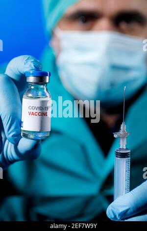 Médecin avec des capuchons médicaux et des gants en latex prend le vaccin covid avec une seringue dans un tableau avec plusieurs flacons Banque D'Images