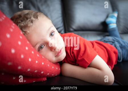 Jeune garçon ennuyé posé sur le canapé rêvant de jour sur les coussins et oreillers relaxant portrait de style de vie réfléchi regardant la télévision seule Banque D'Images