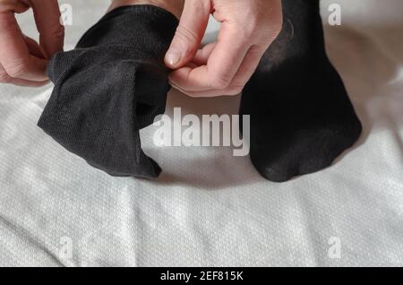 Les mains d'un homme adulte mettent de nouvelles chaussettes. Un homme à la maison le matin met des chaussettes grises sur sa jambe. Cliquez. Mise au point sélective Banque D'Images