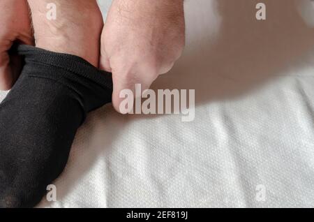 Les mains d'un homme adulte mettent de nouvelles chaussettes. Un homme à la maison le matin met des chaussettes grises sur sa jambe. Cliquez. Mise au point sélective Banque D'Images