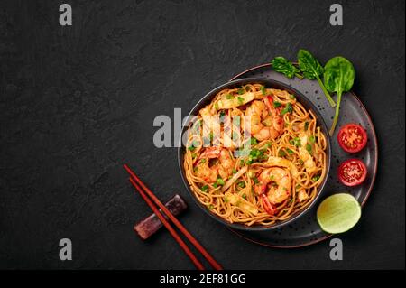 Mie Goreng dans un bol noir sur une table en ardoise sombre. Cuisine indonésienne nouilles de crevettes et légumes sautés. Cuisine asiatique. Vue de dessus. Copier l'espace Banque D'Images