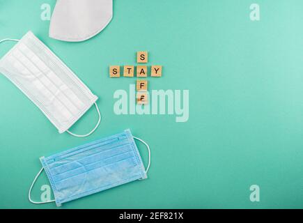 Mot Restez en sécurité. Masques médicaux. L'expression est en lettres de bois. Vue de dessus. Motivation. Arrière-plan bleu. Copier l'espace Banque D'Images
