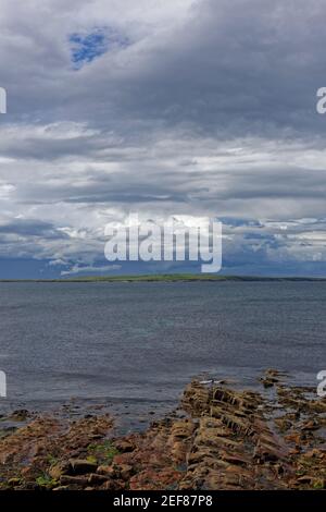 Vue sur l'île de stroma, une partie des Orkneys de la plage rocheuse de John OÕGroats avec des nuages de pluie sombres à l'horizon. Banque D'Images