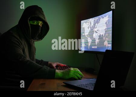 Pirate masqué regardant la caméra utilise un ordinateur pour organiser une attaque massive de violation de données dans le monde entier. Concept de cyber-criminel. Banque D'Images