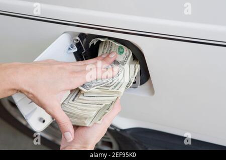 Gros plan sur les mains d'un personnage qui a mis la monnaie papier américaine dans un réservoir d'essence d'une voiture Banque D'Images