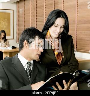 Homme d'affaires et femme d'affaires assis dans un bureau et regardant dans un magazine Banque D'Images