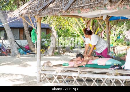 Un voyageur masculin ayant un massage sur la plage, Koh Phangan, Thaïlande Banque D'Images