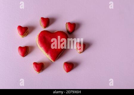 Gros cookie cœur rouge et petits cookies autour isolés sur fond violet avec espace de copie pour le texte ou le design. Concept Saint Valentin et amour Banque D'Images