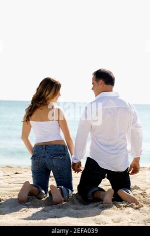 Vue arrière d'un homme adulte moyen et d'un jeune femme à genoux en tenant les mains sur la plage Banque D'Images