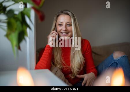 Portrait d'une jeune fille souriante qui fait un appel téléphonique avec son ami. C'est l'hiver et elle est assise sur le canapé Banque D'Images