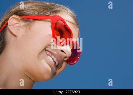 Vue à angle bas d'une fille portant des lunettes de soleil rouges et sourire Banque D'Images