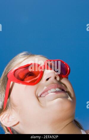 Vue à angle bas d'une fille portant des lunettes de soleil rouges et sourire Banque D'Images