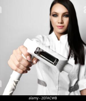 Jeune femme brune médecin cosmetologiste en uniforme médical montre écran laser d'équipement médical Banque D'Images