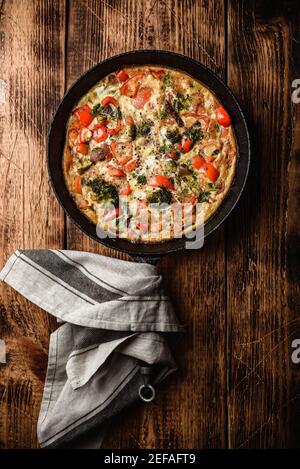 Frittata aux légumes avec le brocoli, le poivron rouge et les herbes dans la poêle en fonte. Vue de dessus Banque D'Images